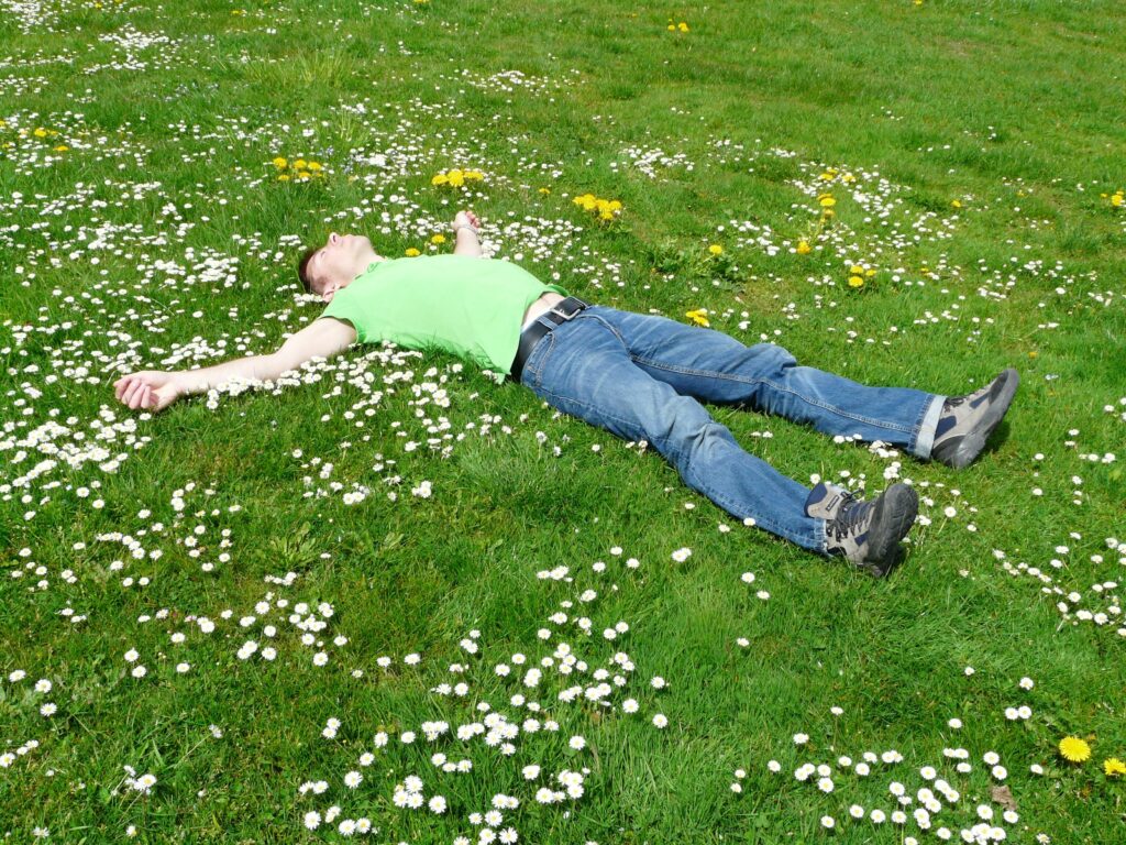 A man lies peacefully in a flowered meadow, embodying relaxation and summer joy.